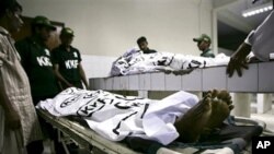 Pakistani rescue workers gather around bodies of shooting victims at a local hospital in Karachi, 17 Oct. 2010.