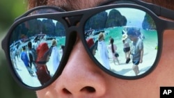 FILE - In this Thursday, May 31, 2018, photo, tourists are reflected in sunglasses on Maya Bay on Phi Phi island in Krabi province, Thailand. 