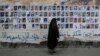 FILE - A Bahraini woman walks past images of political prisoners plastered on a wall in Sanabis, Bahrain, Oct. 22, 2015. In May 2018, the court revoked the citizenship of 115 people in a mass terrorism trial.