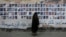 FILE - A Bahraini woman walks past images of political prisoners plastered on a wall in Sanabis, Bahrain, Oct. 22, 2015. In May 2018, the court revoked the citizenship of 115 people in a mass terrorism trial.