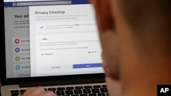 FILE - A man poses a photo in front of a computer showing Facebook ad preference pages, in San Francisco, California, March 26, 2018.