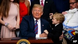 President Donald Trump hugs Jordan McLinn, a Duchenne muscular dystrophy patient, after signing "right to try" legislation in the South Court Auditorium on the White House campus, May 30, 2018, in Washington.