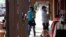 A server wears a face covering while delivering a drink to a patron sitting in an outside dining area at a restaurant as shoppers head into a store amid the coronavirus pandemic, Aug. 4, 2020, in Grand Lake, Colo. 