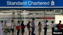People queue up outside a Standard Chartered Bank branch before operation hours at the central business district in Singapore January 23, 2014. Standard Chartered's Chief Executive Peter Sands said takeover talk that has resurfaced around his bank after r