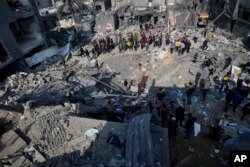 Warga Palestina melihat hancurnya gedung keluarga Al-Gatshan setelah serangan Israel di kamp pengungsi Nusseirat, Jalur Gaza tengah, 18 Desember 2023. (Foto: AP)