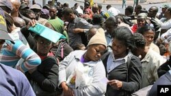 A woman seeks shade beneath her ID documents as she joins about 200 Zimbabweans in a queue outside the Home Affairs offices in downtown Johannesburg, 6 Oct 2010.