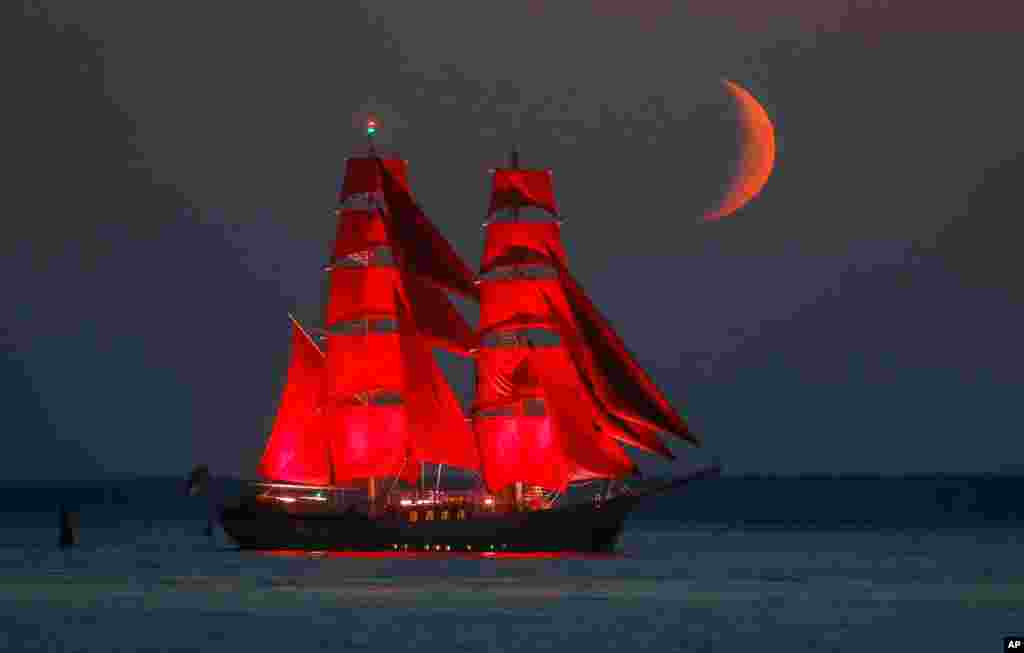 A brig with scarlet sails travels on the Finnish Gulf coast during a rehearsal for the Scarlet Sails festivities marking school graduation which will take place on June 27 in St. Petersburg, Russia, with the setting moon in the background. 