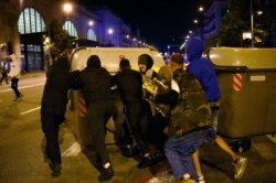 A group of people push a dustbin after a demonstration against curfew and deprivation of rights, in Barcelona, on Oct. 26, 2020. Spain's Catalonia region said it was studying imposing a lockdown on weekends to fight the spread of the coronavirus.