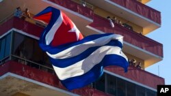 FILE - People watch a concert given by Puerto Rico's Olga Tanon, from a building flying a Cuban flag in Havana, Cuba. U.S. critics of Obama's opening to Cuba have complained the president has received little in return for restoring diplomatic relations with the former Cold War enemy.