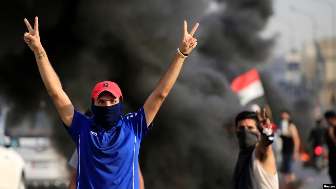 Demonstrators gesture as they block the road with burning tires during a protest over unemployment, corruption and poor public services, in Baghdad, Iraq, Oct. 2, 2019.