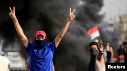 Demonstrators gesture as they block the road with burning tires during a protest over unemployment, corruption and poor public services, in Baghdad, Iraq, Oct. 2, 2019.
