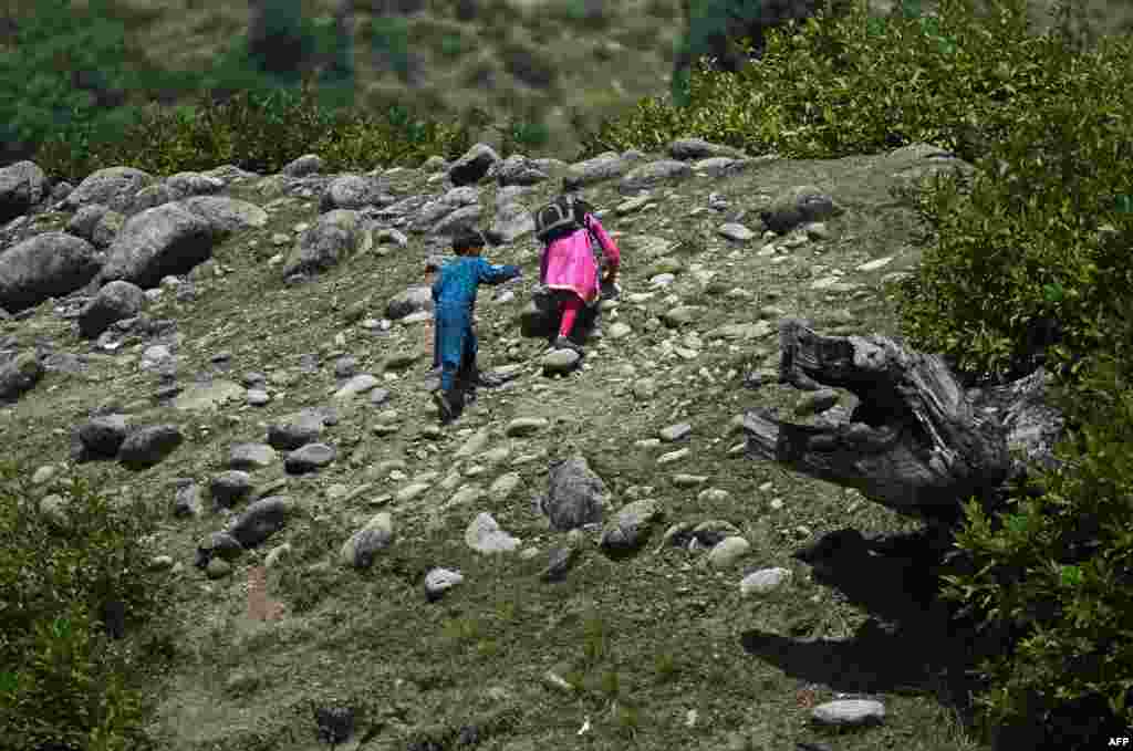 دو بچے اسکول جانے کے لیے اونچائی پر چڑھ رہے ہیں کیوں کہ ان کا عارضی اسکول پہاڑی کی چوٹی پر قائم ہے۔