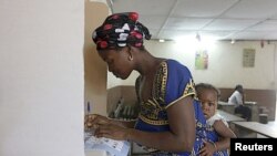 A woman with a baby on her back, votes at a polling station in Abidjan, Ivory Coast, December 11, 2011.