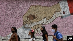 Jóvenes con mascarillas pasan frente a un mural de mosaico con la imagen de una mano depositando una boleta, en Caracas, Venezuela, el domingo. Octubre 11, de 2020.