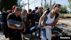 Des réfugiés syriens portent un des leurs compagnons tombé malade au cours de leur traversée de la Grèce à la Mécedoine, 12 septembre 2015.