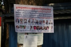 A banner displaying photos of the 18 senior CNRP leaders wanted for arrest is plastered on a tree in Poipet, Banteay Meanchey province, on Nov 7, 2019. (Sun Narin/VOA Khmer)