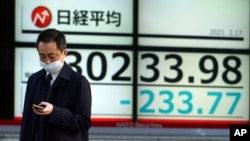 A man wearing a protective mask walks in front of an electronic stock board showing Japan's Nikkei 225 index at a securities firm, Feb. 17, 2021, in Tokyo.