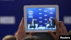 Russia's President Vladimir Putin (R) and Prime Minister Dmitri Medvedev are seen on the screen of a tablet computer during a meeting in the Moscow region, Oct. 3, 2013.