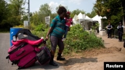 FILE - A pregnant mother who said she was from Haiti and her daughter are watched by Royal Canadian Mounted Police officers as they prepare to cross the U.S.-Canada border into Hemmingford, Quebec, from Champlain, N.Y.