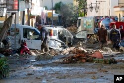 Orang-orang membersihkan lumpur dan puing-puing setelah hujan deras memicu tanah longsor yang meruntuhkan bangunan dan menyebabkan sebanyak 12 orang hilang, di Casamicciola, di Pulau Ischia, Italia selatan, Minggu, 27 November 2022. (Foto: AP)