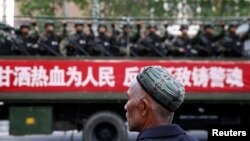 Seorang pria Uighur melihat truk berisi polisi paramiliter melintas di jalan di Urumqi, Xinjiang. (Foto: Dok)