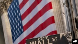 FILE - A Wall Street sign is seen against the background of a giant American flag hanging on the building of the New York Stock Exchange, in New York City, Sept. 21, 2020.