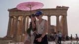 FILE - Tourists with an umbrella walk in front of the Parthenon at the ancient Acropolis in central Athens, June 12, 2024. (AP Photo/Petros Giannakouris, File)