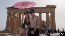 FILE - Tourists with an umbrella walk in front of the Parthenon at the ancient Acropolis in central Athens, June 12, 2024. (AP Photo/Petros Giannakouris, File)