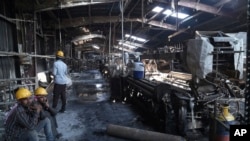 FILE - Indian laborers sit near burnt remains after a fire broke out at Nandan Denim, one of the largest denim suppliers in the world, in Ahmedabad, India, Feb. 9, 2020.