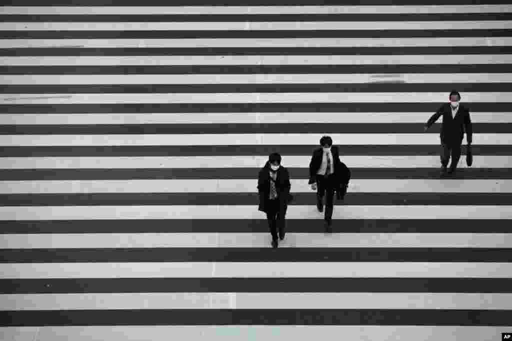 Commuters wearing masks walk across a pedestrian crosswalk in Tokyo, Japan.