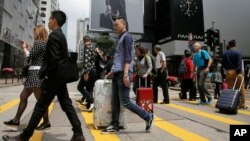 FILE - Mainland Chinese tourists carry suitcases as they walk at a shopping district in Hong Kong, April 12, 2015.