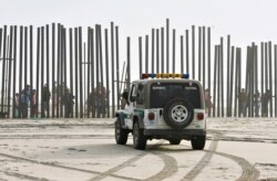 Un vehículo de la Patrulla Fronteriza permanece estacionado frente a un grupo de personas que mira desde el otro lado de la cerca limítrofe entre México y Estados Unidos en la zona conocida como…