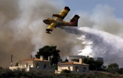 A firefighting plane drops water over a fire near holiday homes in Costa village in the Argolida region, in Southeastern Greece during a developing wild fire, July 20, 2015.