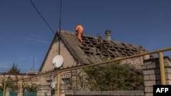 Hombres reparan el techo de una casa que resultó dañada durante un ataque ruso nocturno, en la ciudad sureña de Kherson, el 30 de octubre de 2023, en medio de la invasión rusa de Ucrania. (Foto de Román PILIPEY / AFP)