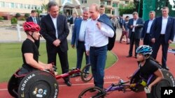 FILE - Russian President Vladimir Putin, center, speaks with athletes of the Russian Paralympic cycling team as he visits a sports training center in Sochi, the Black Sea resort that hosted this year's Winter Olympics, Russia, Oct. 23, 2014. 