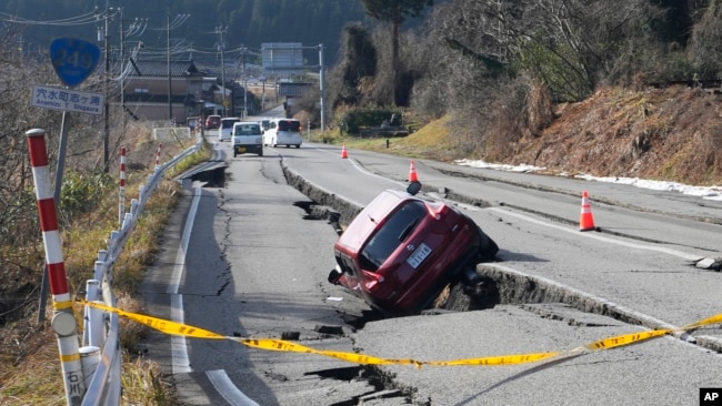 A car is trapped at a partially collapsed road caused by a powerful earthquake near Anamizu Town, Ishikawa Prefecture Tuesday, Jan. 2, 2024.