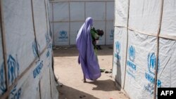 FILE - A woman carries her baby through temporary shelters provided by the Mission for the United Nations in Maiduguri, Nigeria, Dec. 7, 2016.