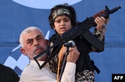 Pemimpin Hamas Yahya Sinwar menggendong anak seorang pejuang Brigade Al-Qassam, yang tewas dalam pertempuran baru-baru ini dengan Israel, dengan senapan Kalashnikov di tangannya selama unjuk rasa di Kota Gaza pada 24 Mei 2021. (Foto: AFP)