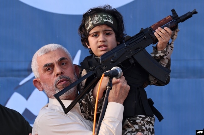 Pemimpin Hamas Yahya Sinwar menggendong anak seorang pejuang Brigade Al-Qassam, yang tewas dalam pertempuran baru-baru ini dengan Israel, dengan senapan Kalashnikov di tangannya selama unjuk rasa di Kota Gaza pada 24 Mei 2021. (Foto: AFP)