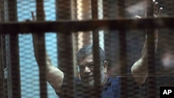 Presiden Mesir terguling, Mohammed Morsi di balik kaca di akademi polisi nasional di pinggiran timur Kairo, Mesir, Sabtu, 16 Mei 2015. Pengadilan Mesir menetapkan keputusan mati atas Presiden Mohammed Morsi. (AP Photo/Ahmed Omar)