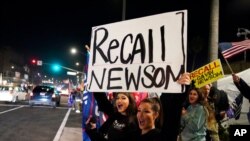 FILE - Demonstrators shout slogans while carrying a sign calling for a recall on Governor Gavin Newsom, in Huntington Beach, Calif., Nov. 21, 2020.