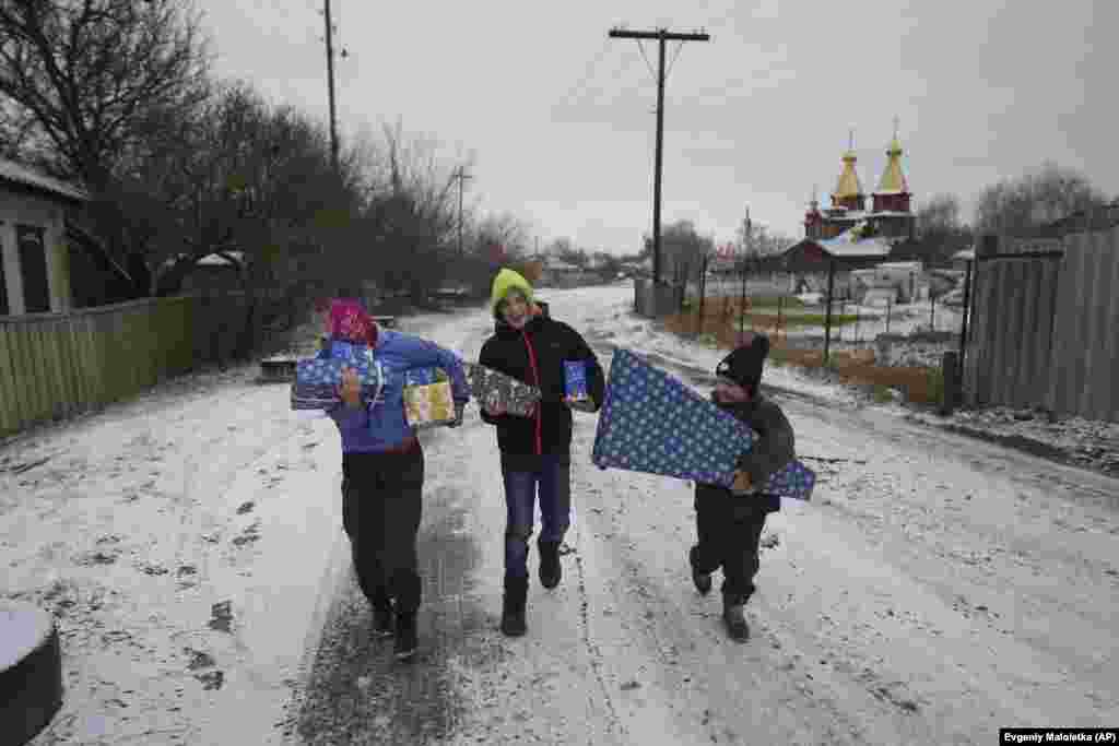 De izquierda a derecha, Masha, de 12 años, Tymofiy, de 12 años, e Illia, de 6, llevan regalos a sus casas después de las celebraciones del Día de San Nicolás en Izium, Ucrania, el 6 de diciembre de 2024.