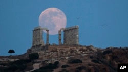 FILE - Seagulls fly as the full moon rises behind the ancient marble Temple of Poseidon at Cape Sounion, southeast of Athens. The latest disbursement of funds will consist of a 1.1 billion euro allotment to be used for servicing debt based on Greece’s successful implementation of 15 financial milestones, and another 1.7 billion euros to help pay back various unpaid debts.