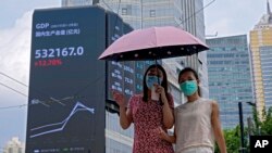 Dua pejalan kaki mengenakan masker, berjalan di dekat papan iklan elektronik yang menunjukkan indeks Produk Domestik Bruto (PDB) China di gedung perkantoran komersial di Shanghai, China, 24 Agustus 2021. (AP Photo/Andy Wong, File)