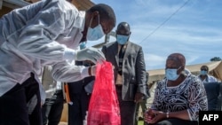 A pharmaceutical expert (L) opens a pack of expired COVID-19 AstraZeneca vaccines to show to Malawi’s Health Minister Khumbize Kandodo Chiponda (R) before they are destroyed in a pharmaceutical incinerator, May 19, 2021. 