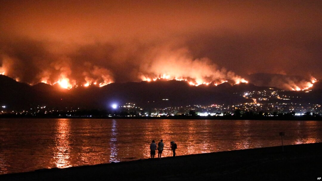 Onlookers are silhouetted against the reflection of a wildfire burning in the Cleveland National Forest in Lake Elsinore, Calif., Aug. 8, 2018. 