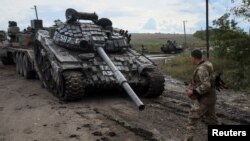 Припадник на украинската армија поминува покрај нефункционален руски тенк во градот Изјум