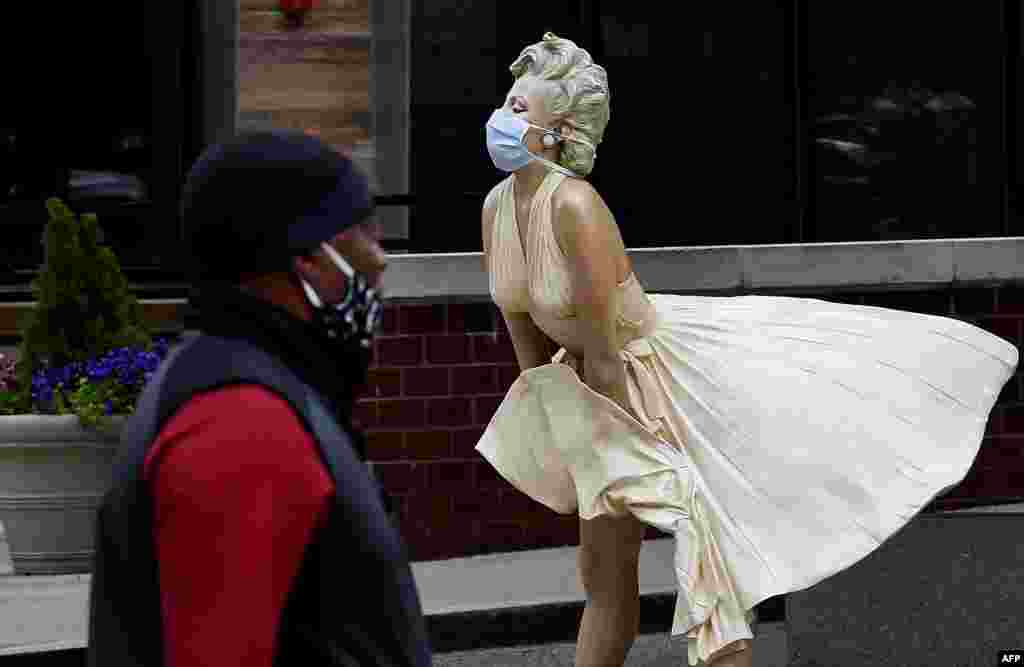 Човек со маска покрај скулптура на Мерилин Монро која исто така има маска во Мериленд. (Olivier DOULIERY / AFP)