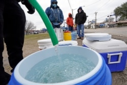 A water bucket is filled as others wait in near-freezing temperatures to use a hose from public park spigot Feb. 18, 2021, in Houston.