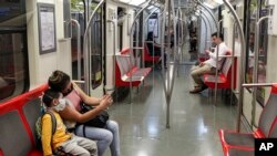 Una mujer y un niño con mascarillas como precaución contra un nuevo coronavirus se toman un selfie dentro de un metro casi vacío en Santiago, Chile, el viernes 20 de marzo de 2020. 